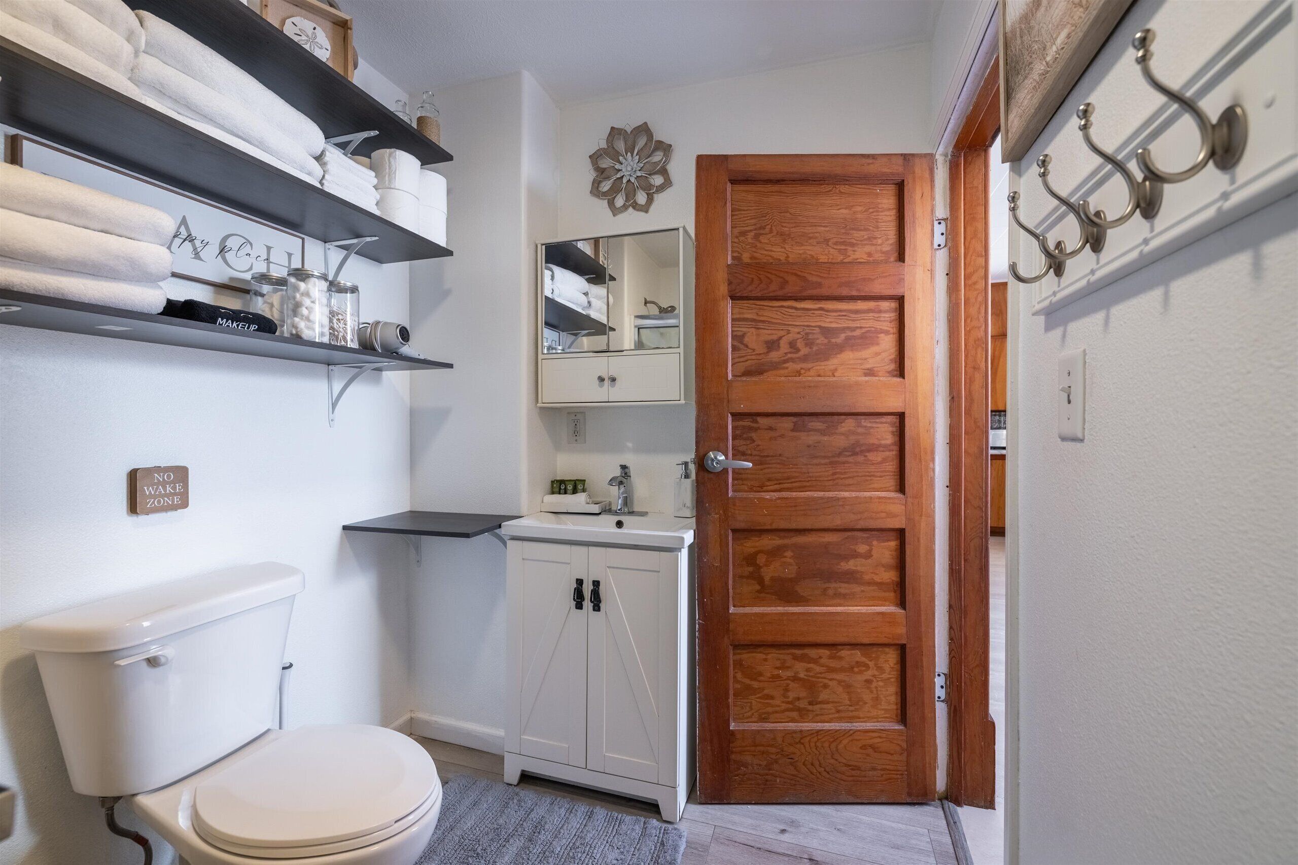 Une petite salle de bain comprenant des toilettes, des meubles blancs, un miroir et une porte en bois.