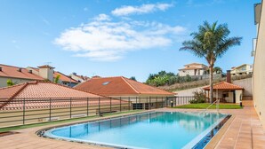 A swimming pool with a tiled deck, surrounded by a fence and palm trees. - Freitas House by Homie (Canhas)