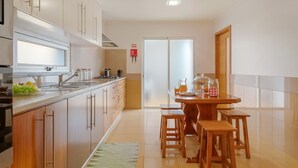 A modern kitchen with wooden cabinets, a stainless steel sink, and a dining area with wooden stools. - Freitas House by Homie (Canhas)