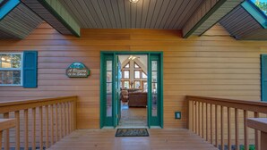 Una terraza de madera que conduce a una cabaña con una puerta verde, un letrero que dice 'A Blessing in da Skies' y una vista al interior.