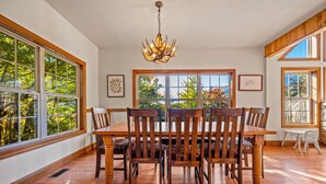Un comedor con una mesa y sillas de madera, ventanas amplias y una araña.