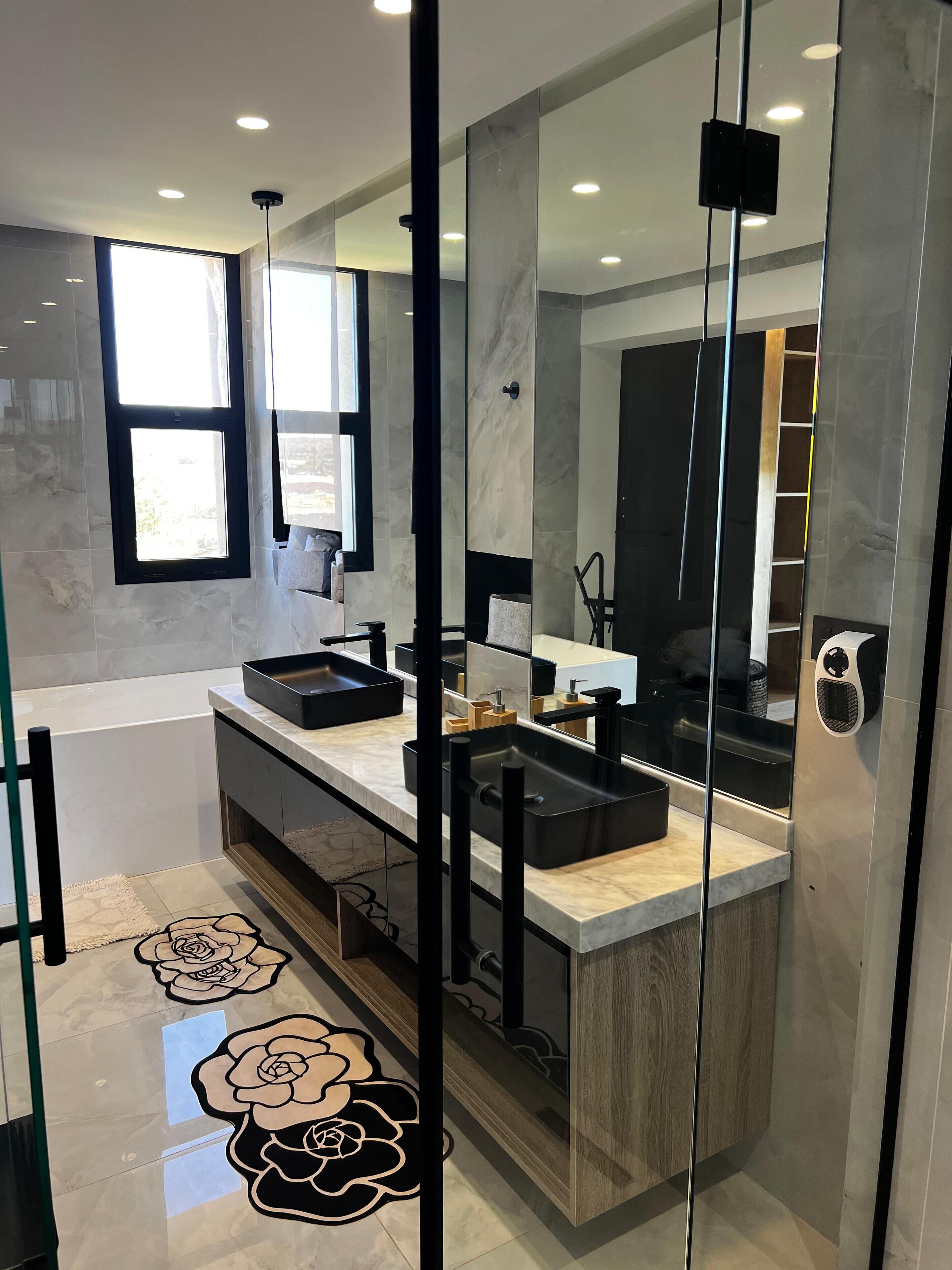 A modern bathroom with a glass partition, a large mirror, and a vanity with two sinks.