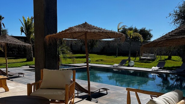 A poolside area with lounge chairs and a table, surrounded by palm trees and a clear blue sky. - Villa Octagon-with private pool&Heated Jacuzzi-13 min from center Essaouira  (Essaouira)