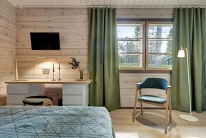 Et værelse med seng, skrivebord, stol, fjernsyn og et vindue med gardiner.