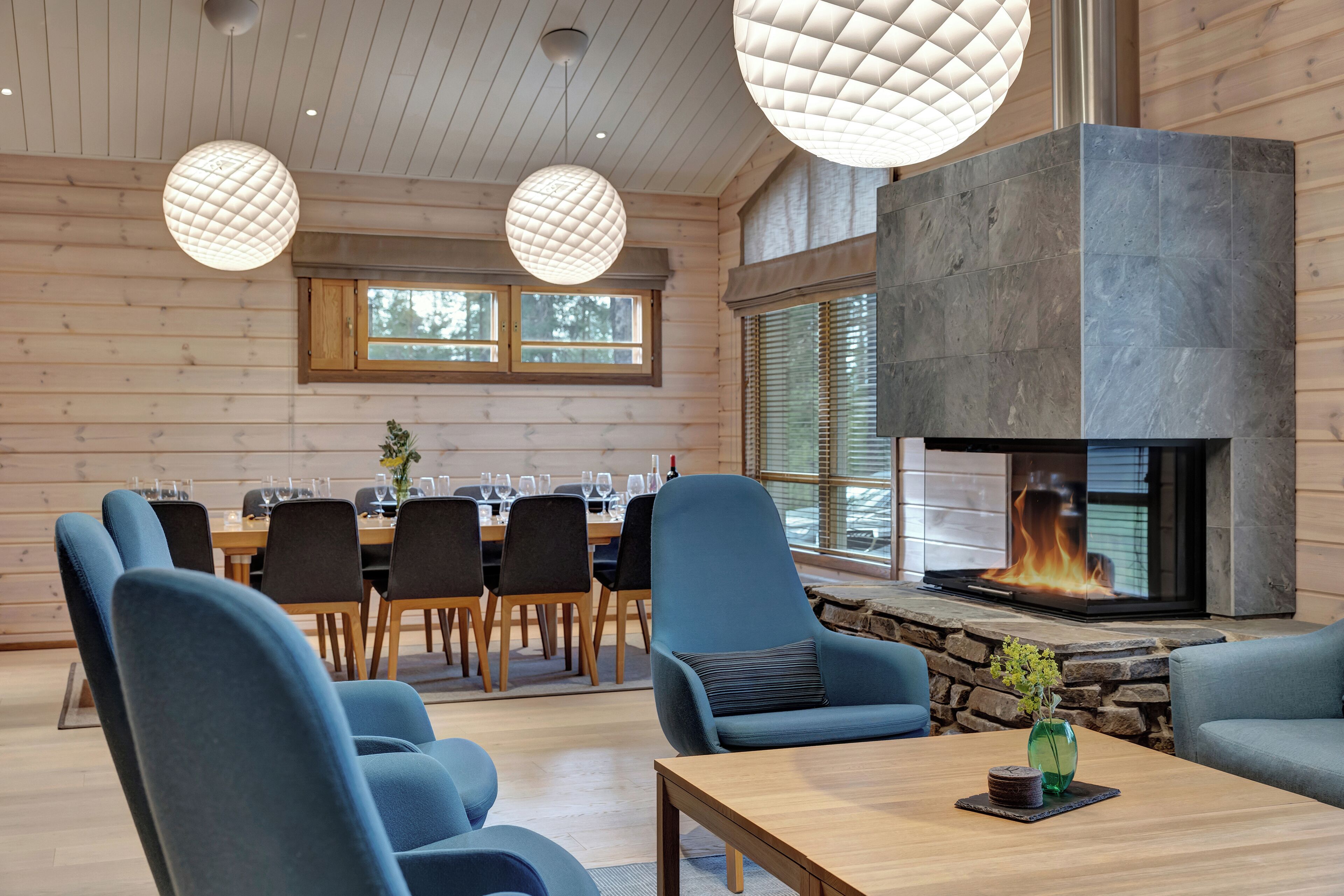 A modern interior with a stone fireplace, wooden walls, and a dining area with chairs and tables.
