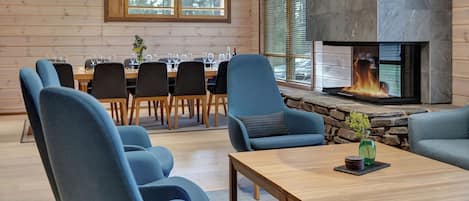 A modern interior with a stone fireplace, wooden walls, and a dining area with chairs and tables.