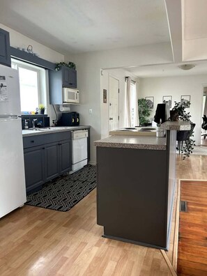 Una cocina moderna con gabinetes grises, un refrigerador blanco, un microondas y una pequeña isla con encimera oscura.