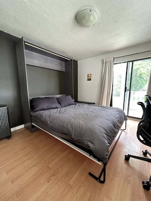 Et moderne værelse med seng, radiator, et vindue med gardiner og en stol.