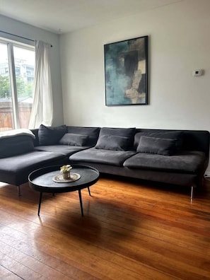 A modern living room with a sectional sofa, a round coffee table, and a large abstract painting on the wall.