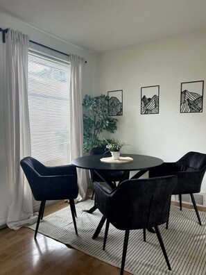 Spiseplads med et rundt bord, sorte stole og en potteplante.