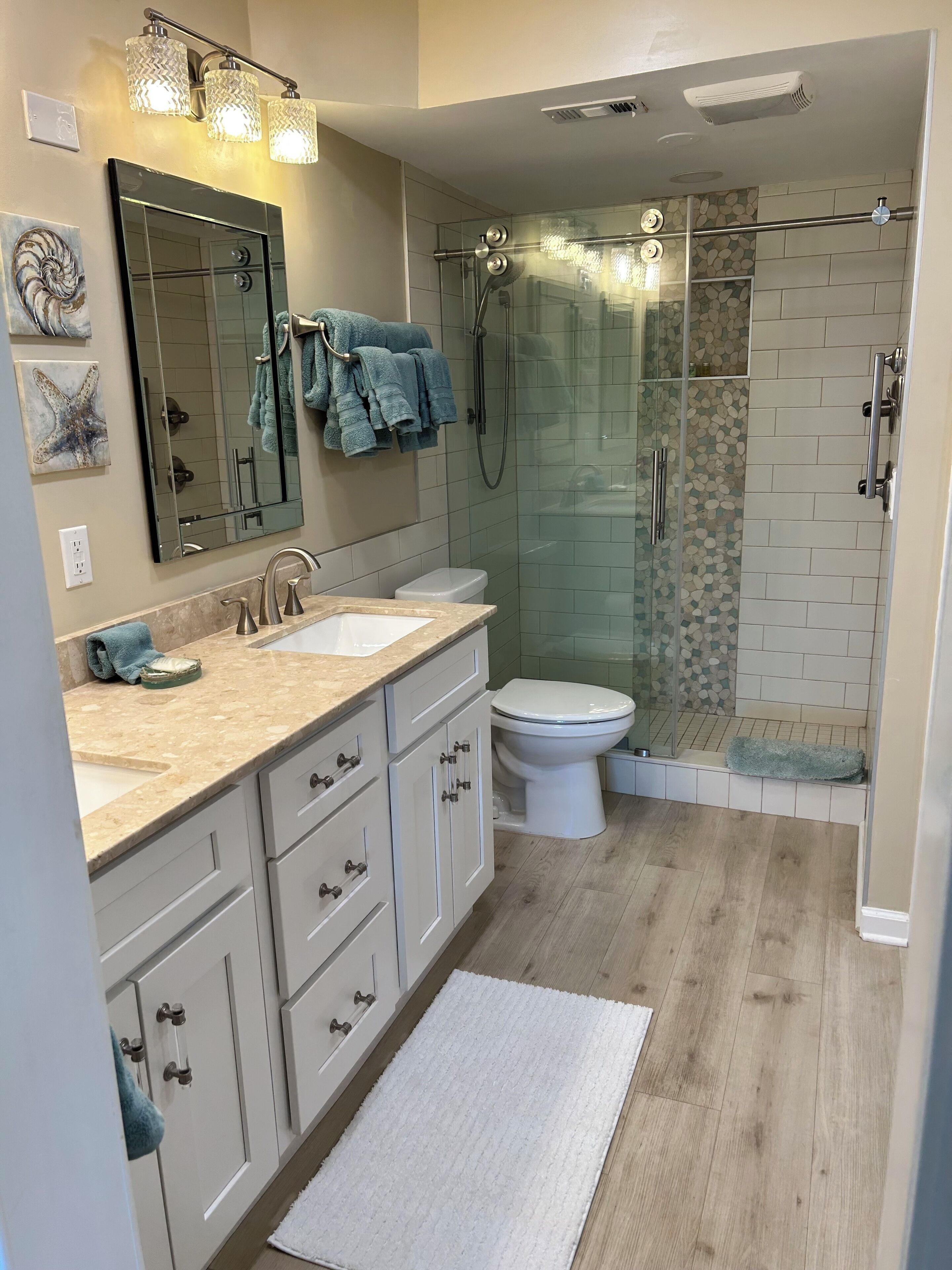 A modern bathroom with a glass-enclosed shower, a large mirror, and a vanity with a sink and cabinet.