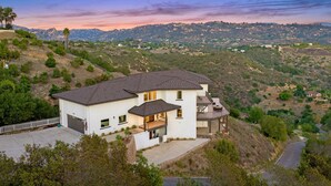 A two-story house with a large garage, a covered patio, and a view of a hilly landscape.