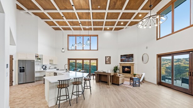 A spacious kitchen with a large island, wooden flooring, and a high ceiling with exposed beams.