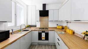A compact kitchen with white cabinetry, a wooden countertop, a black range hood, and a yellow appliance. - Charming Central Leicester 4 Bed Accommodation (Leicester)