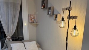 Een slaapkamer met een bed, een vloerlamp, een raam met gordijnen en een wandplank met decoratieve objecten.