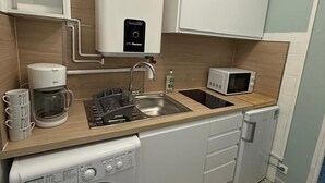 Een praktische keuken met een wasmachine, koffiezetapparaat, magnetron en spoelbak.