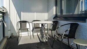 Ein kleiner Sitzbereich im Freien mit einem runden Tisch und vier Stühlen, einem Fenster mit Jalousien und einer Betonwand.