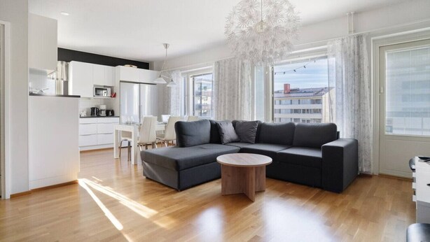 Ein modernes Wohnzimmer mit einer Eckcouch, einem runden Couchtisch und einem Essbereich mit weißem Tisch und Stühlen.