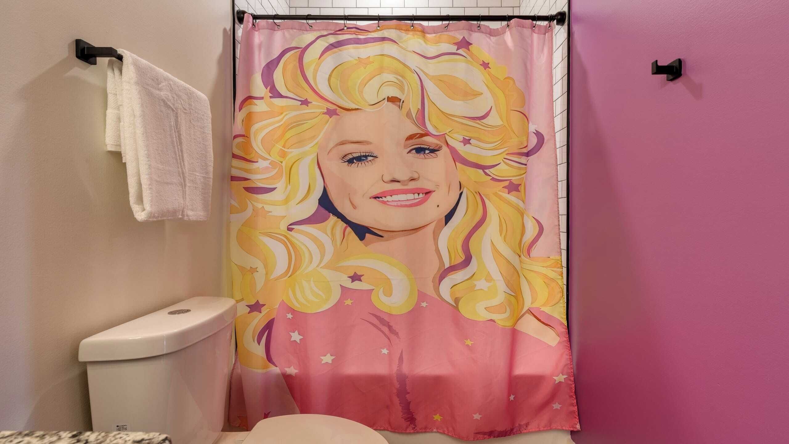 Un baño con una pared rosa, un inodoro blanco y una cortina de ducha de diseño colorido.
