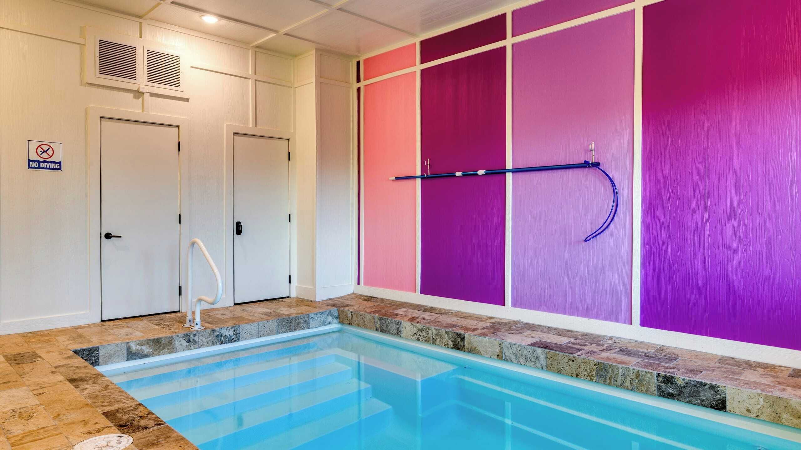 A swimming pool with a tiled deck, a no diving sign, and a wall with a purple and pink color scheme.