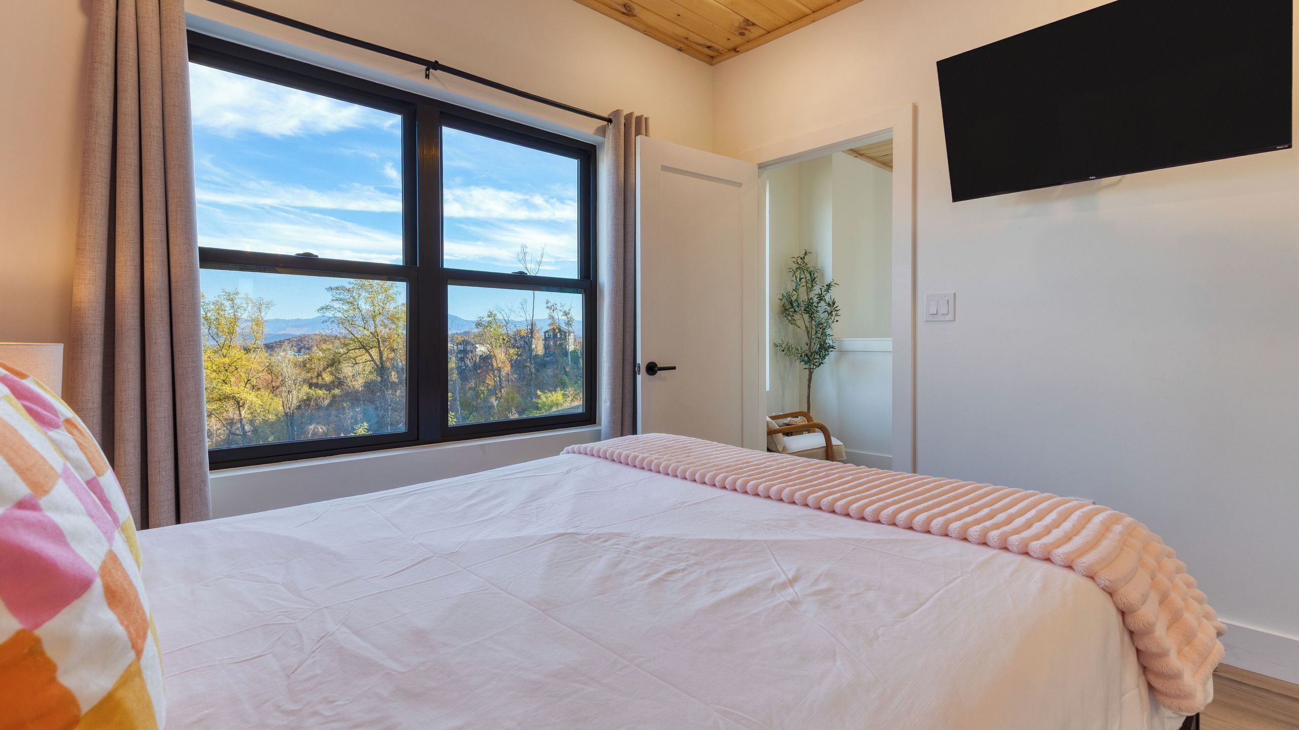 A bedroom with a large window, a bed, a bedside table, and a mirror.