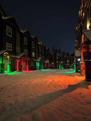 Een met sneeuw bedekte straat 's nachts, huizen verlicht met kleurrijke lichtjes.