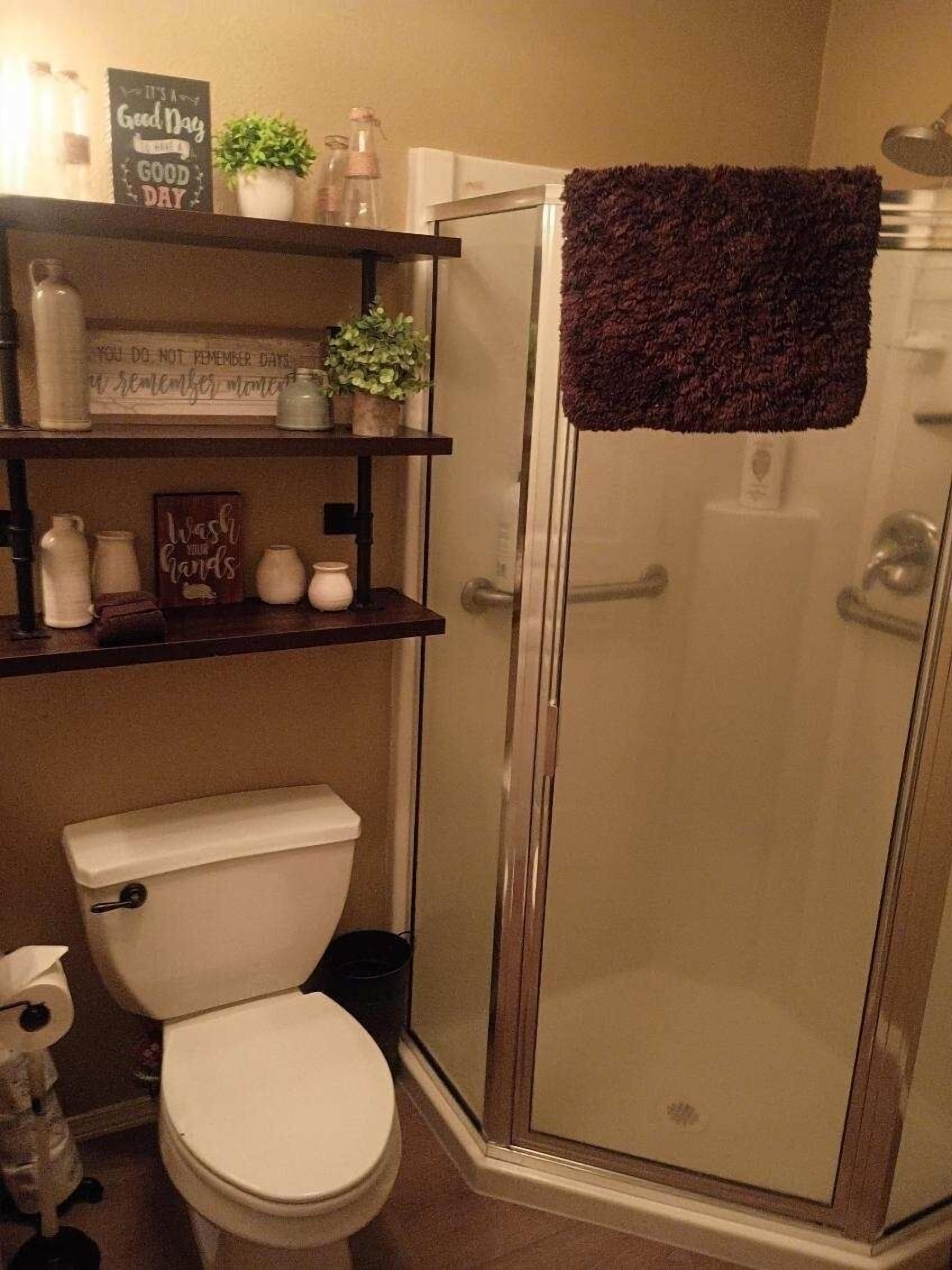 A bathroom with a toilet, a glass shower enclosure, and shelves with toiletries.