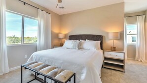 Quarto com uma cama grande, duas mesas de cabeceira com luminárias, um banco e um ventilador de teto.
