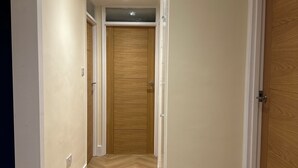 A hallway with wooden flooring, white walls, and a wooden door at the end. - Beautiful 2 bedroom apartment in fantastic central location close to High Street (Sutton)