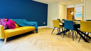 A modern living room with a yellow sofa, blue walls, and a dining area with yellow chairs and a wooden table. - Beautiful 2 bedroom apartment in fantastic central location close to High Street (Sutton)