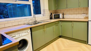 A compact kitchen with green cabinets, a microwave, a sink, and a washing machine. - Beautiful 2 bedroom apartment in fantastic central location close to High Street (Sutton)