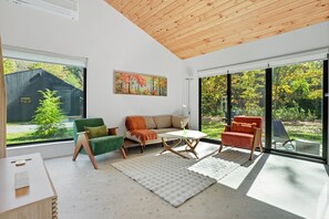A modern living room with a wooden ceiling, large windows, a sofa, chairs, and a painting. - Loft 3 - Designer Cabin, Walls of Light, Sauna (West Windsor)