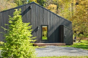 A modern, dark-colored building with a single visible door and a small porch area. - Loft 3 - Designer Cabin, Walls of Light, Sauna (West Windsor)