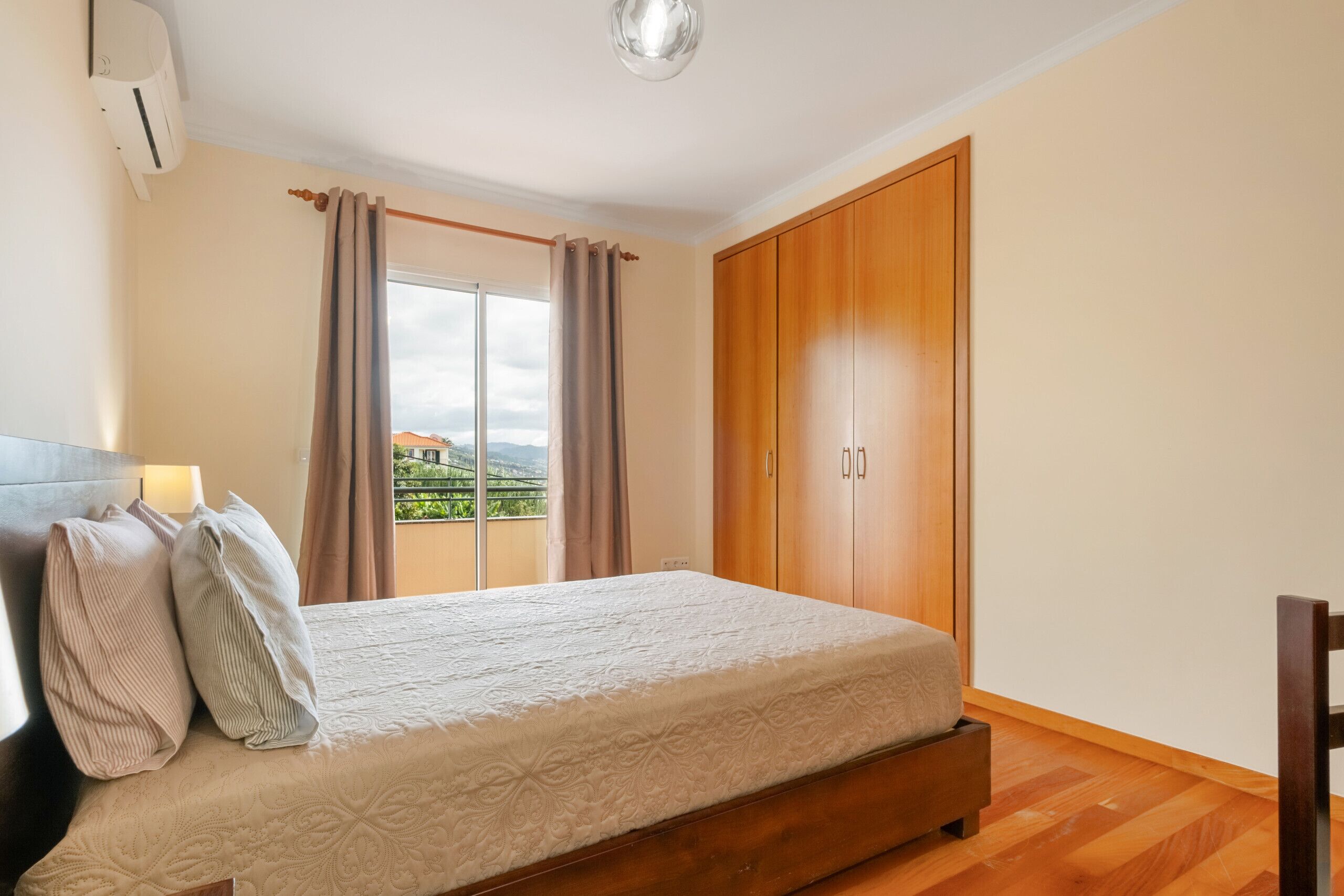 A bedroom with a bed, curtains, a wardrobe, and a view of the outdoors.