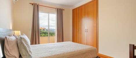 A bedroom with a bed, curtains, a wardrobe, and a view of the outdoors.