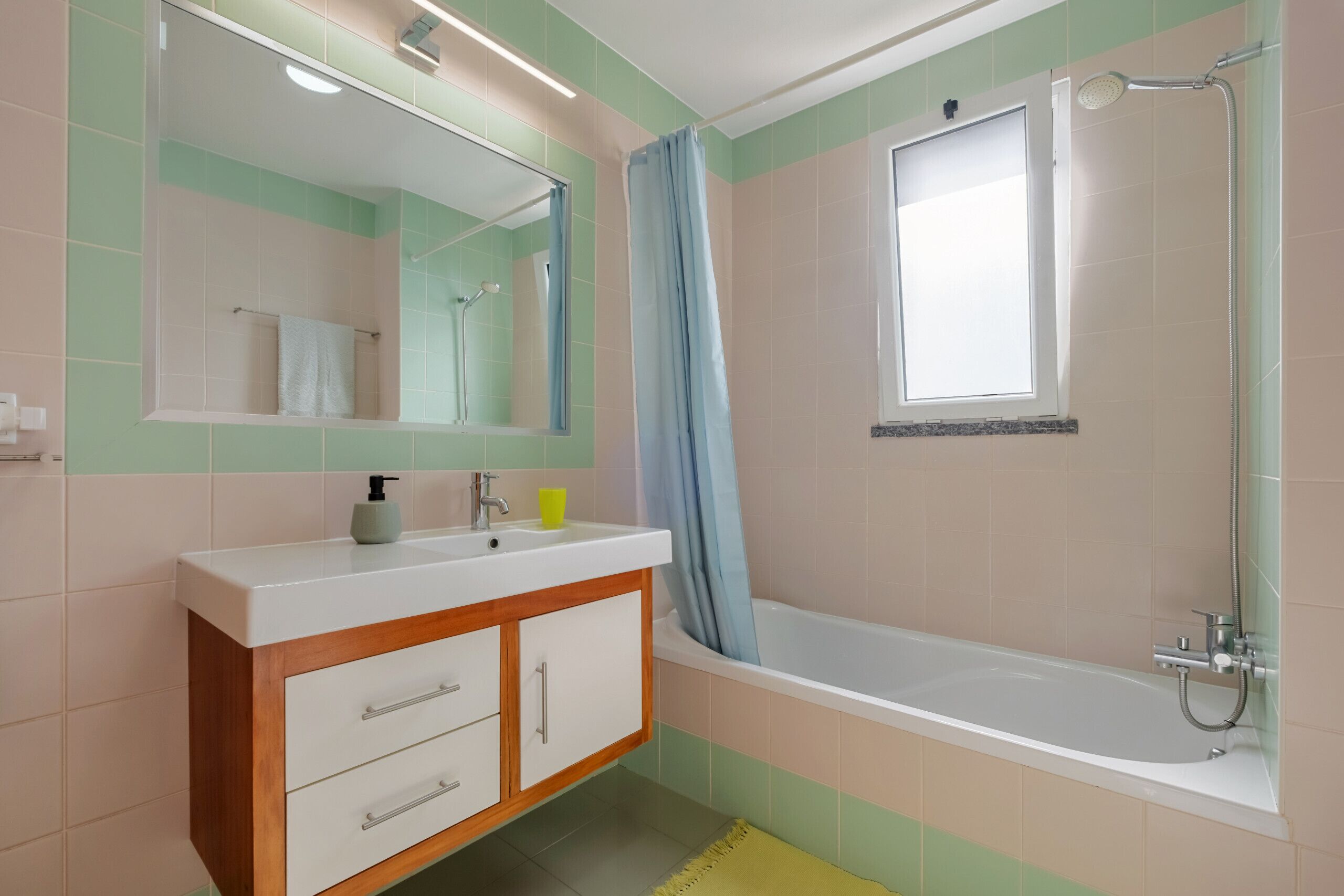 A bathroom with a white sink, wooden cabinet, mirror, and a bathtub with a showerhead.