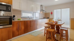 A modern kitchen with wooden cabinets, stainless steel appliances, and a dining area with wooden stools. - Freitas House by Homie (Ponta do Sol)