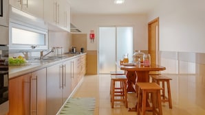 A modern kitchen with wooden cabinets, a stainless steel sink, and a dining area with wooden stools. - Freitas House by Homie (Ponta do Sol)