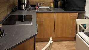 Une cuisine compacte avec des meubles en bois, un plan de travail noir, une cuisinière encastrée, un évier et un four à micro-ondes.
