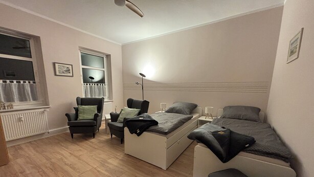 Une petite pièce comprenant un lit, deux chaises, un bureau et un radiateur.