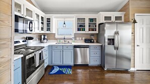 A modern kitchen with white cabinets, stainless steel appliances, and a blue rug. - Private Beachfront Home with Ocean Views & Pool (Surfside)