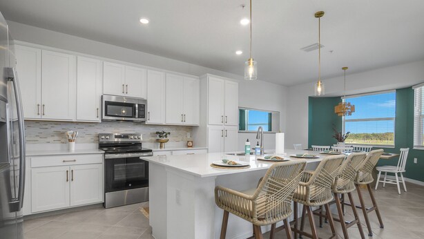 A modern kitchen with white cabinetry, stainless steel appliances, a large island with bar stools, and a view of the outdoors through a window. - Top-Floor Babcock Ranch Condo Near Fort Myers • Pool, Golf, SW Florida (Punta Gorda)