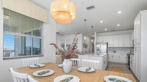 A modern kitchen with white cabinets, a central island, and a dining area with a wooden table and white chairs. - Top-Floor Babcock Ranch Condo Near Fort Myers • Pool, Golf, SW Florida (Punta Gorda)