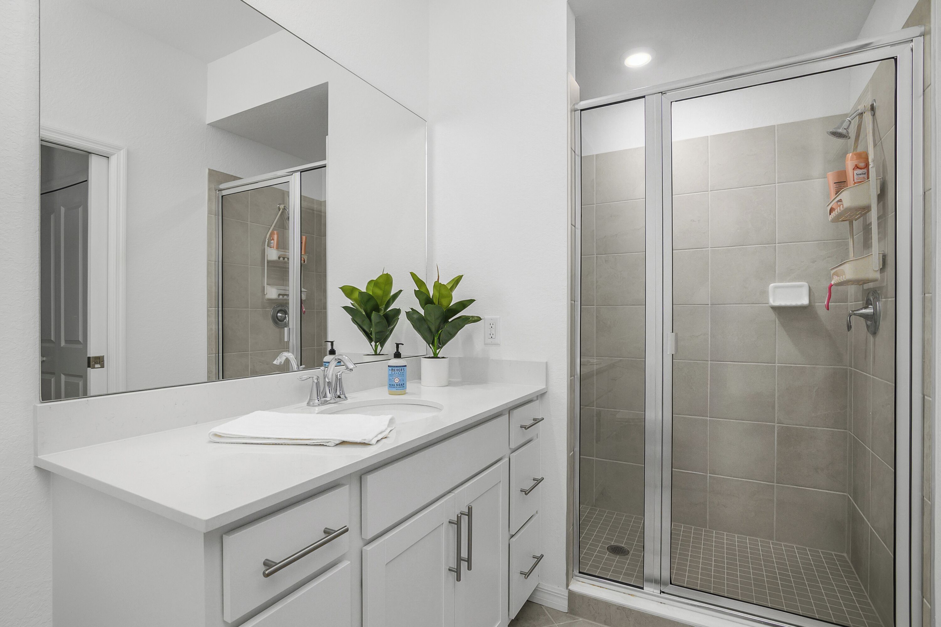 A modern bathroom with a white vanity, a glass shower enclosure, and a large mirror.