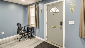Ein Zimmer mit Tür, Schreibtisch mit Stuhl und Fenster mit Vorhängen.