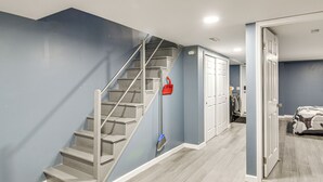 Eine Treppe mit Handlauf, ein roter Feuermelder und eine Tür zu einem Zimmer mit einem Bett.