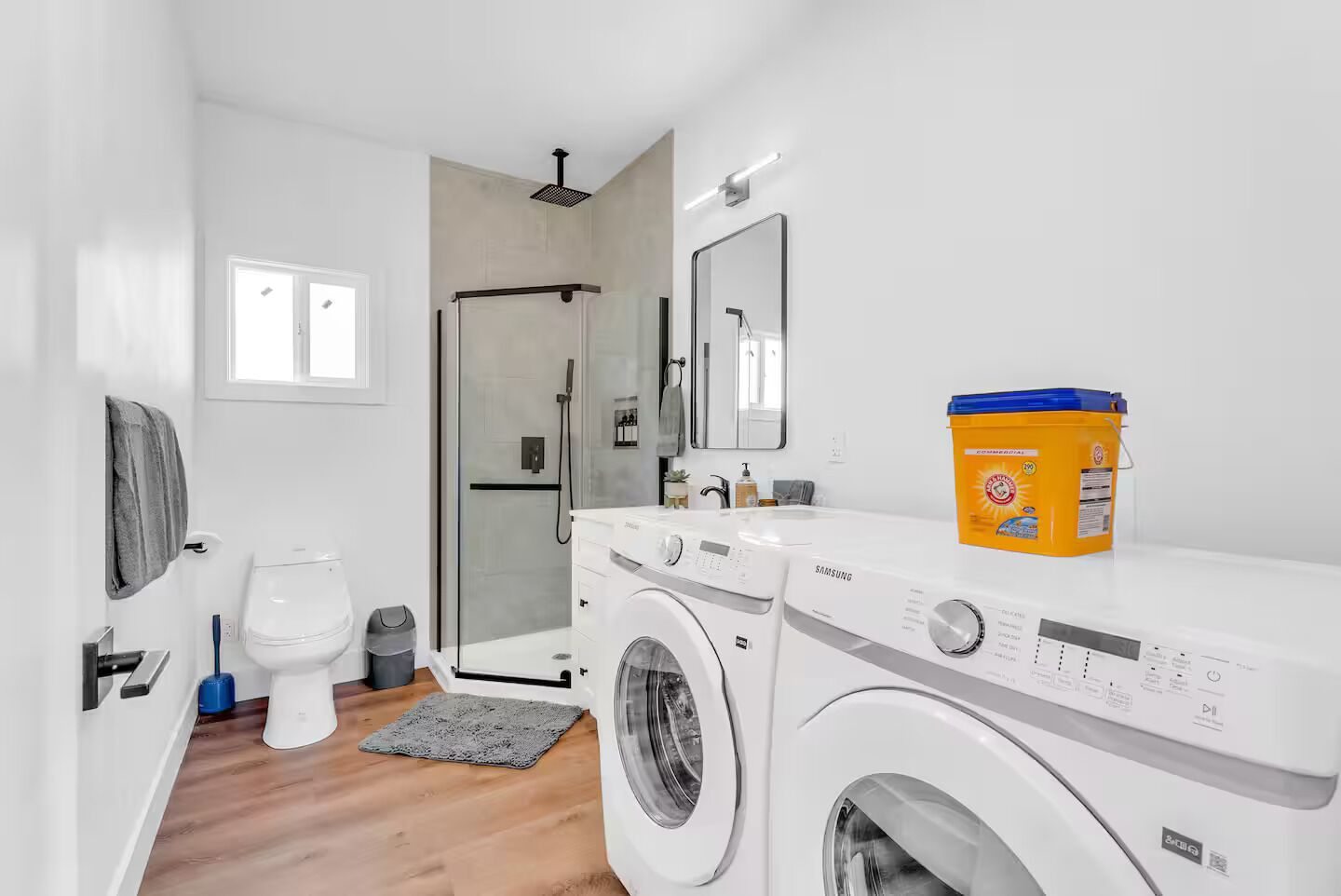 A modern bathroom with a washing machine, a toilet, a shower, and a large mirror.
