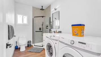 A modern bathroom with a washing machine, a toilet, a shower, and a large mirror.