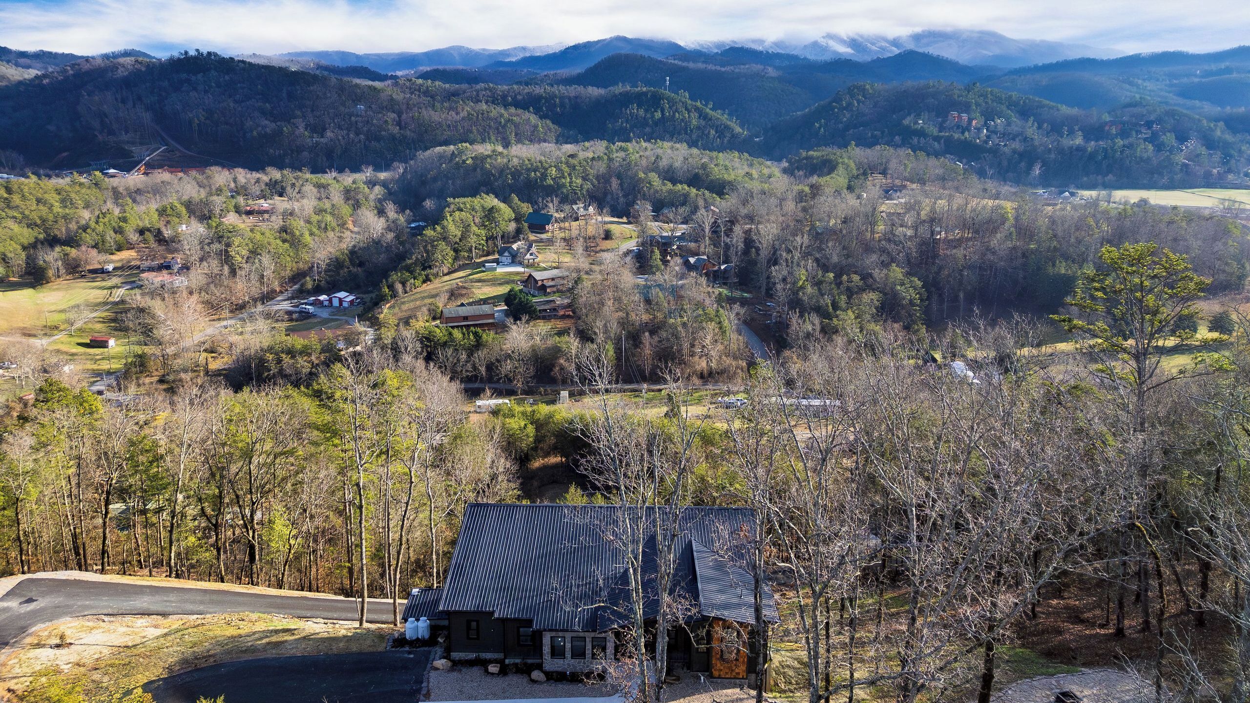 A rural landscape with a small building featuring a metal roof, surrounded by trees and hills.
