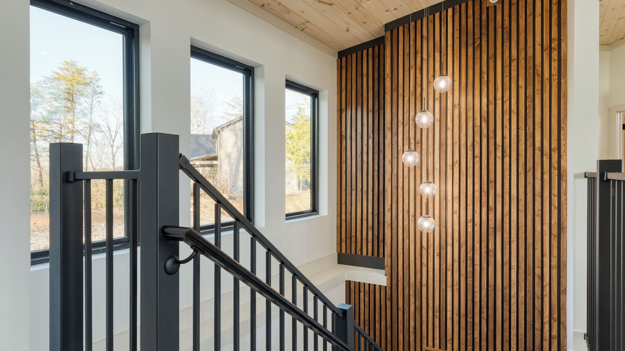 A staircase with black railings, wooden panel wall, and multiple windows.